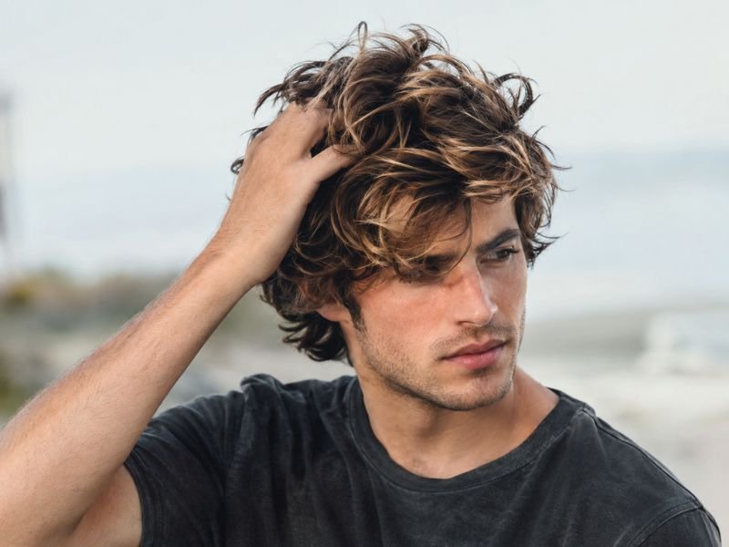 Man styling surfer haircut with fingers for texture